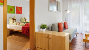 A modern living room with a sofa, a wooden cabinet, and a bed with colorful bedding. - Apartment Alicia by Interhome (Grächen)