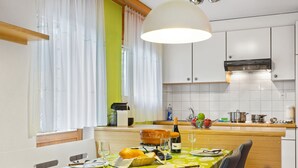 A modern kitchen with white cabinets, a dining table with a green leaf-patterned tablecloth, and a large pendant light. - Apartment Alicia by Interhome (Grächen)