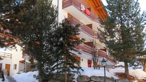 A multi-story building with balconies, surrounded by snow-covered ground and trees. - Apartment Alicia by Interhome (Grächen)