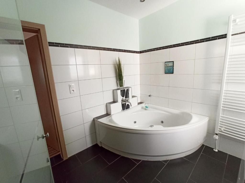 Een badkamer met een groot bad, witte betegelde muren, een kleine potplant en een handdoekhouder.