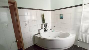 Een badkamer met een groot bad, witte betegelde muren, een kleine potplant en een handdoekhouder.