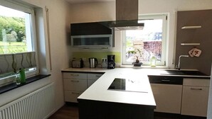 A modern kitchen with a central island, built-in microwave, and a window with a view of greenery. - Urlaub in Ländlicher Umgebung (Illschwang)