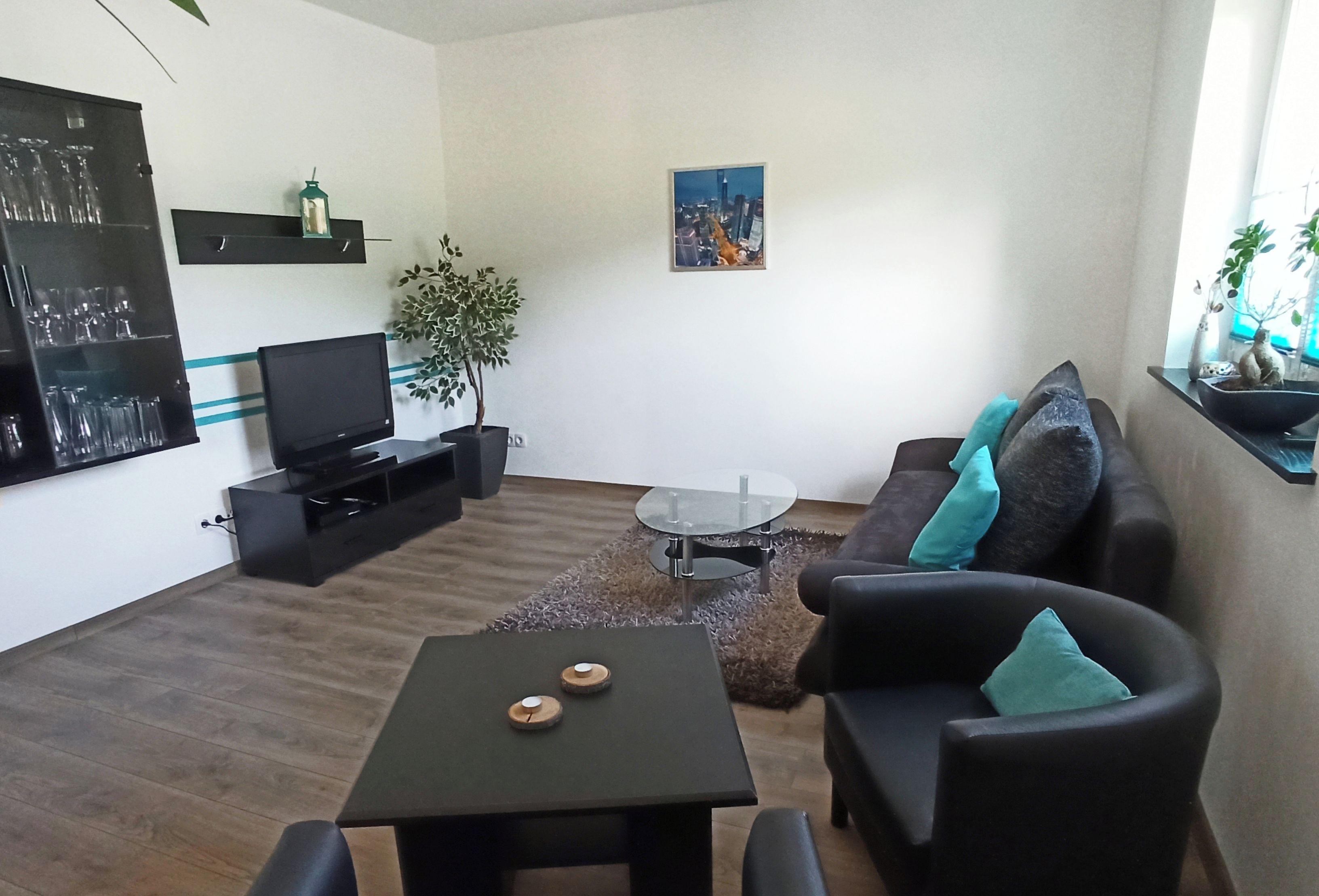 A modern living room with a flat-screen TV, a coffee table, a sofa, and a small table with two candles.