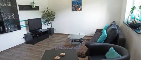 A modern living room with a flat-screen TV, a coffee table, a sofa, and a small table with two candles.