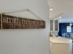 A wooden sign with coordinates on a white wall in a room with a white countertop and cabinets. - Charming Lakefront Condo at Bernard's Landing, only steps from the shore! (Moneta)
