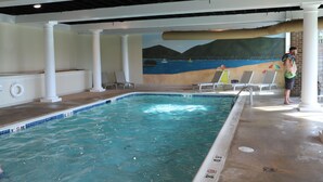 An indoor swimming pool with a mural of a beach scene, lounge chairs, and a lifeguard stand.