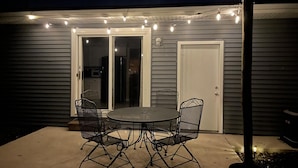 An outdoor patio with a round table and four chairs, a sliding glass door, and string lights.