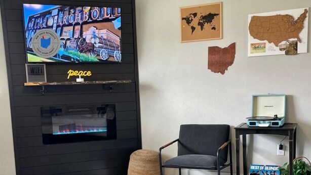 A modern living room with a flat-screen TV mounted on a black wall, a wooden coffee table, a grey armchair, and a small side table with a record player.