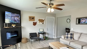 A modern living room with a flat-screen TV, a ceiling fan, a sofa, a coffee table, and a fireplace.
