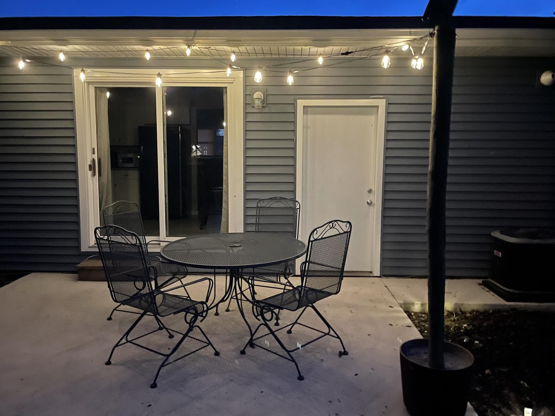 Une terrasse avec une table ronde et quatre chaises, le tout illuminé par des guirlandes lumineuses.