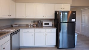 A kitchen with white cabinets, a stainless steel refrigerator, a microwave, and a coffee maker.