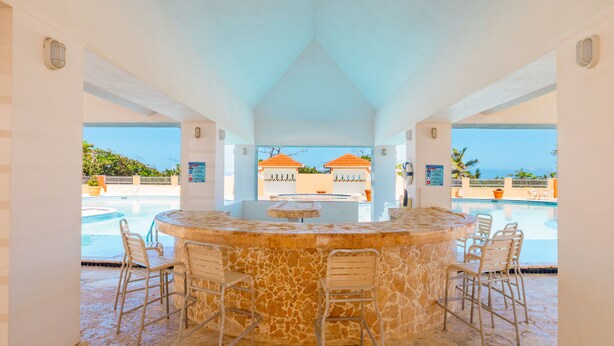 A bar area with a stone counter and four chairs, overlooking a pool with a view of buildings and palm trees. - Golden Dream Studio 306 B (Isabela)