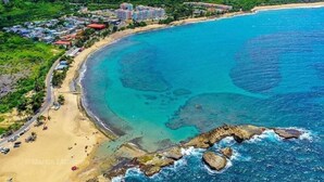 An aerial view of a coastal area with a beach, a road, and residential buildings. - Golden Dream Studio 306 B (Isabela)