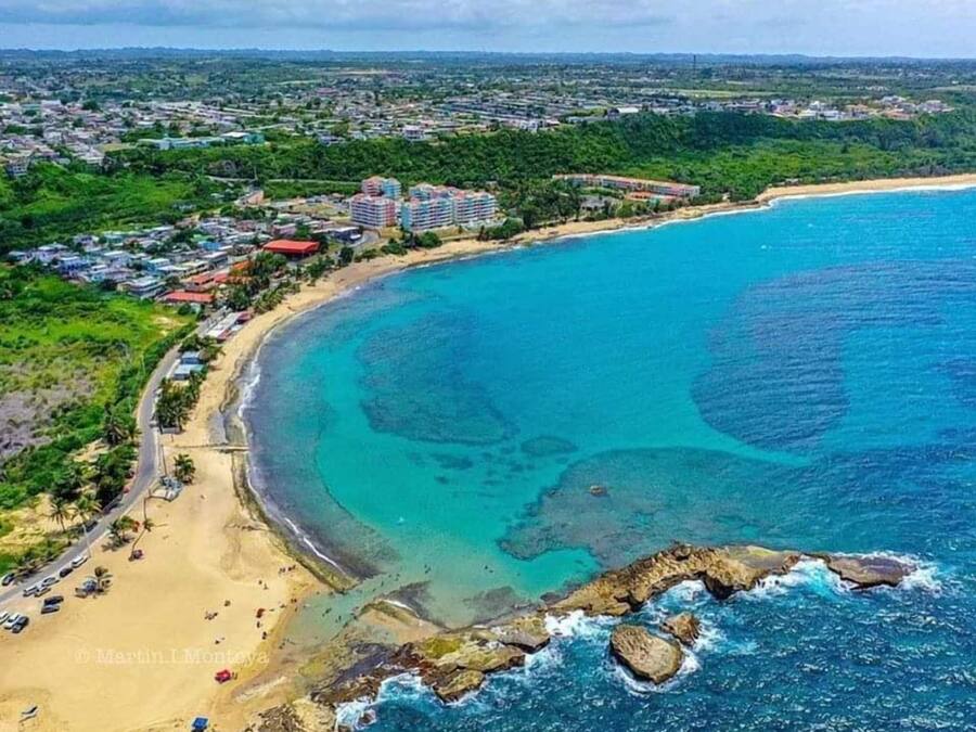 An aerial view of a coastal area with a beach, a road, and residential buildings.