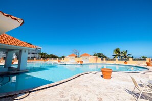 Une piscine dotée d’une terrasse carrelée, entourée de bâtiments aux toits orange et de palmiers.