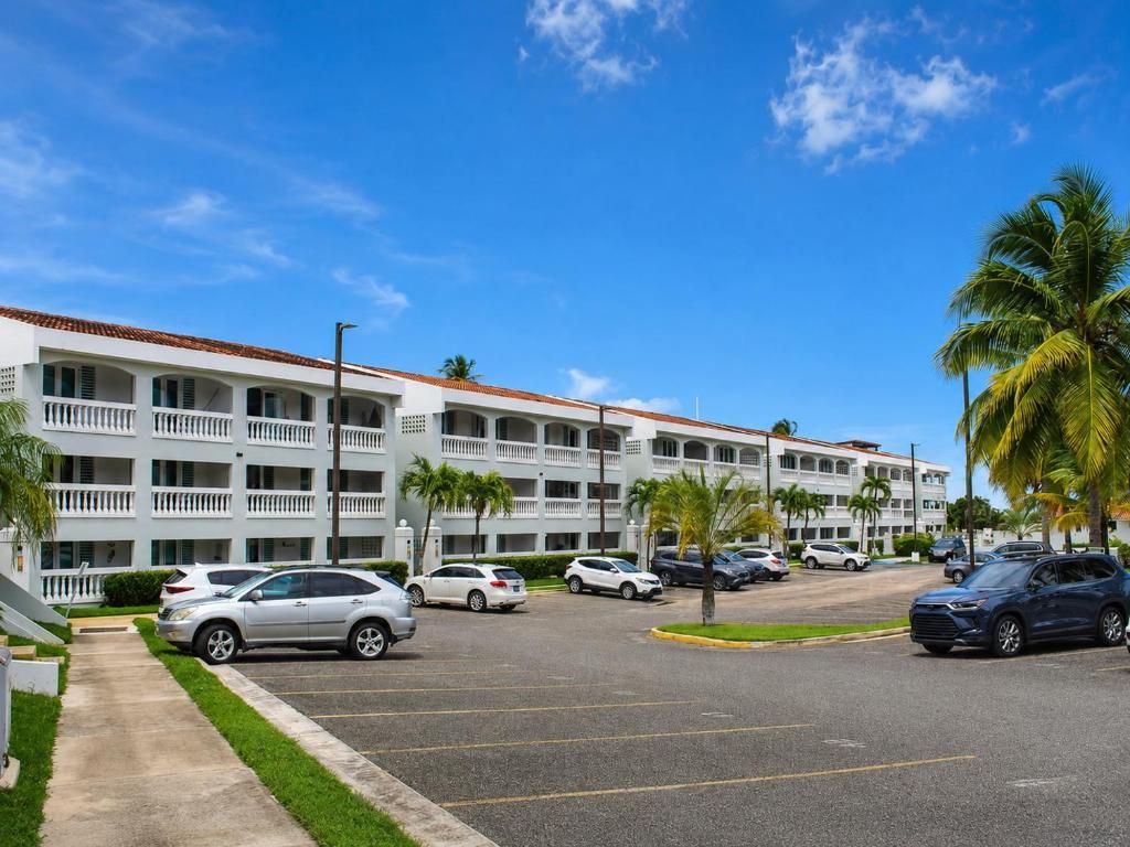 A multi-story hotel with a parking lot, palm trees, and a clear blue sky.