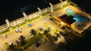 An aerial view of a hotel with a swimming pool, multiple parking spaces, and a landscaped area with palm trees. - Golden Dream Studio 306 B (Isabela)