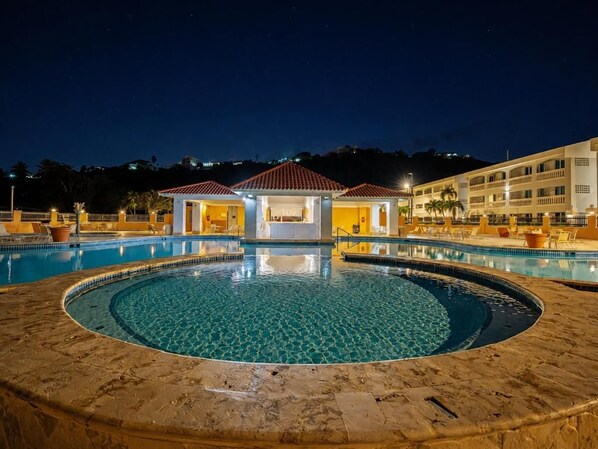Una piscina con diseño circular, un área de descanso techada y un edificio al fondo.