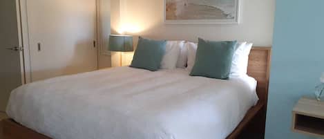 Un letto rifatto con un copriletto bianco e due cuscini, una lampada da comodino e un quadro con una spiaggia sulla parete.