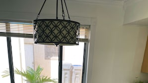 A dining area with a wooden table, black chairs, a hanging light fixture, and a window with blinds. - Hello Sunshine 321.. Lift Off (Titusville)