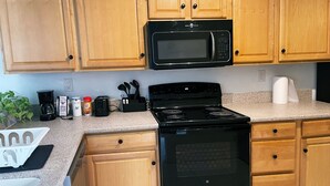 A kitchen with wooden cabinets, a black microwave, a stove, and various kitchen items on the counter. - Hello Sunshine 321.. Lift Off (Titusville)