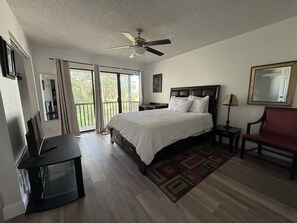Un dormitorio con cama, escritorio, silla, ventilador de techo y vistas al exterior a través de una puerta corredera.