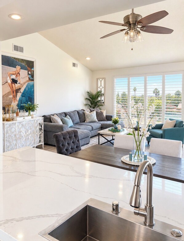 A modern kitchen with a marble countertop, a stainless steel sink, and a ceiling fan.