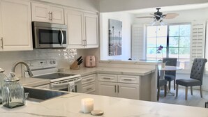 A modern kitchen with white cabinetry, a marble island, and a dining area with a ceiling fan.
