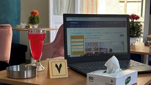Una computadora portátil sobre una mesa de madera, con una caja de pañuelos y un vaso de bebida roja.