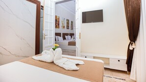Habitación de hotel con cama, baño, armario y televisión en la pared.