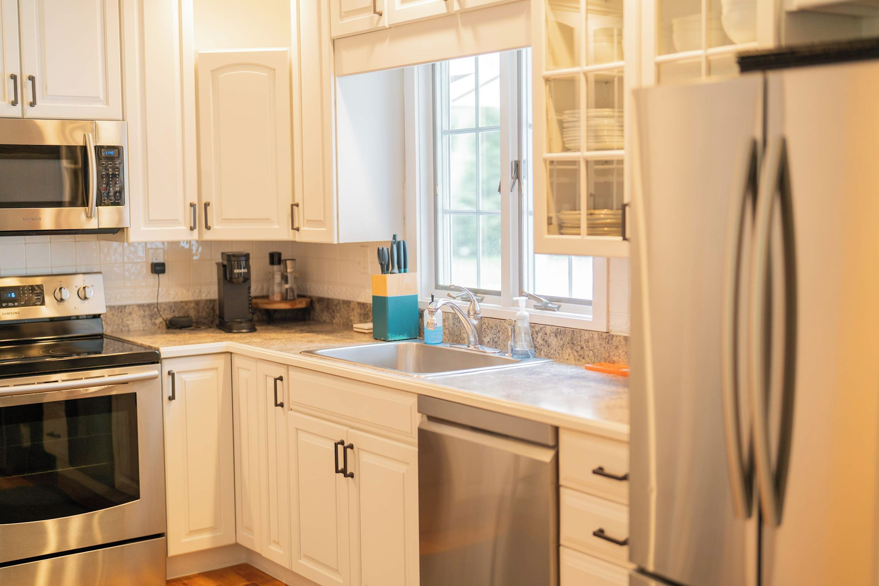 A modern kitchen with stainless steel appliances, white cabinetry, and a window providing natural light.