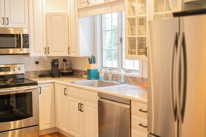 A modern kitchen with stainless steel appliances, white cabinetry, and a window providing natural light. - Southampton Estate w Heated Pool (Southampton)