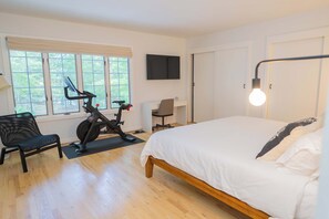 A bedroom with a bed, a desk, an exercise bike, and a chair. - Southampton Estate w Heated Pool (Southampton)
