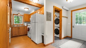 A kitchen with wooden cabinets, a refrigerator, a washing machine, and a window with a view of trees.