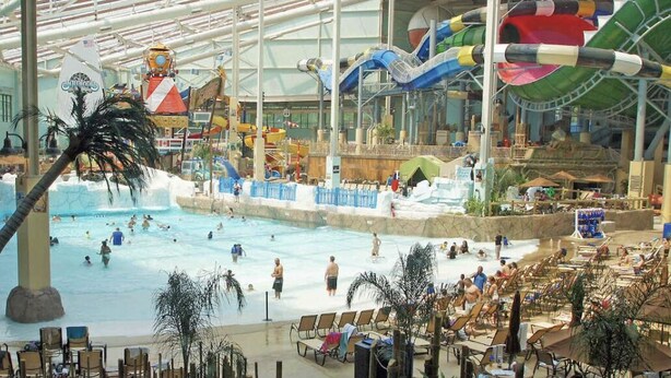Parque acuático interior con una piscina grande, toboganes de agua y zonas de descanso.