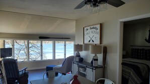 A spacious living room with a large window overlooking a lake, a dining area with a table and chairs, and a cozy seating area with a fireplace. - Lakefront cottage on Silver lake near Letchworth Park (Castile)