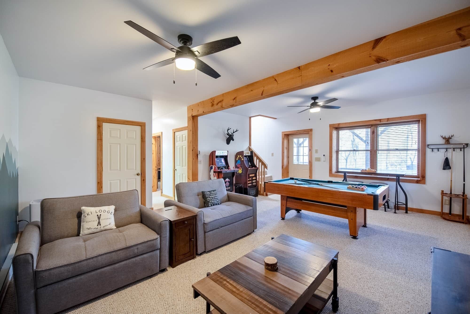 A spacious living area with a pool table, sofas, ceiling fans, and arcade games.