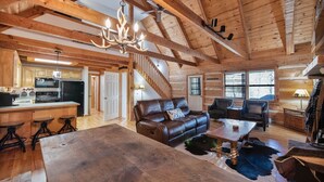 A log cabin interior with a kitchen, living area, and a staircase. - Bear Pause Cabin 3 BR/3BA Amazing Lake View EV Charger (Seven Devils)