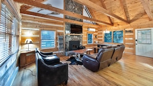 A log cabin interior with a fireplace, leather sofa, and wooden floors. - Bear Pause Cabin 3 BR/3BA Amazing Lake View EV Charger (Seven Devils)