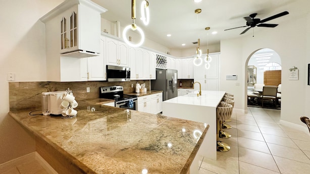 A modern kitchen with white cabinetry, granite countertops, stainless steel appliances, and pendant lighting.