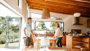 A modern kitchen with wooden cabinets, a dining table, and a large window. - Karu ō te Kiwi (Pākawau)