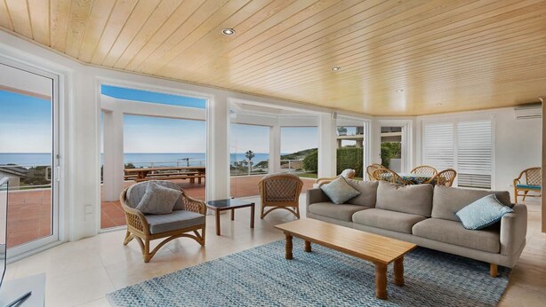 A spacious living room with a large window overlooking the sea, furnished with a sofa, chairs, and a coffee table.