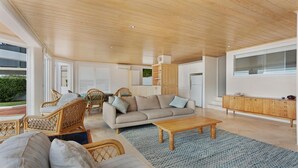A spacious living room with a wooden ceiling, a beige sofa, wicker chairs, and a wooden coffee table.