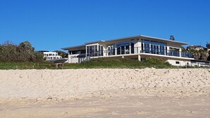 A modern beach house with a flat roof, large windows, and a name sign.