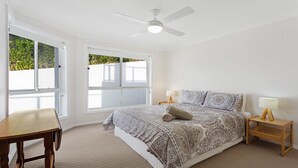 A bedroom with a large bed, two bedside tables, a ceiling fan, and a window with a view of greenery.