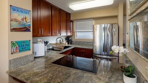 Une cuisine avec des meubles en bois, un réfrigérateur en acier inoxydable, une cuisinière encastrée et une orchidée en pot.