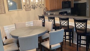 A dining area with a round table and six chairs, a chandelier, wooden cabinets, and a kitchen in the background. - Only 2 miles from shopping, banking, food, entertainment,15 to downtown Atlanta (Lithonia)