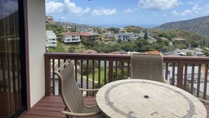 Ein Balkon mit rundem Tisch und zwei Stühlen, mit Blick auf ein Wohngebiet mit Häusern und den Ozean.