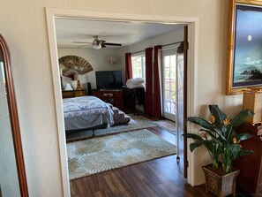 A bedroom with a bed, a desk, a television, a ceiling fan, and a window with curtains.