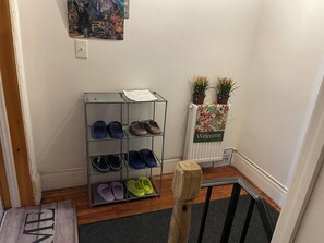 Un pasillo con un zapatero, un cartel de bienvenida y un radiador.